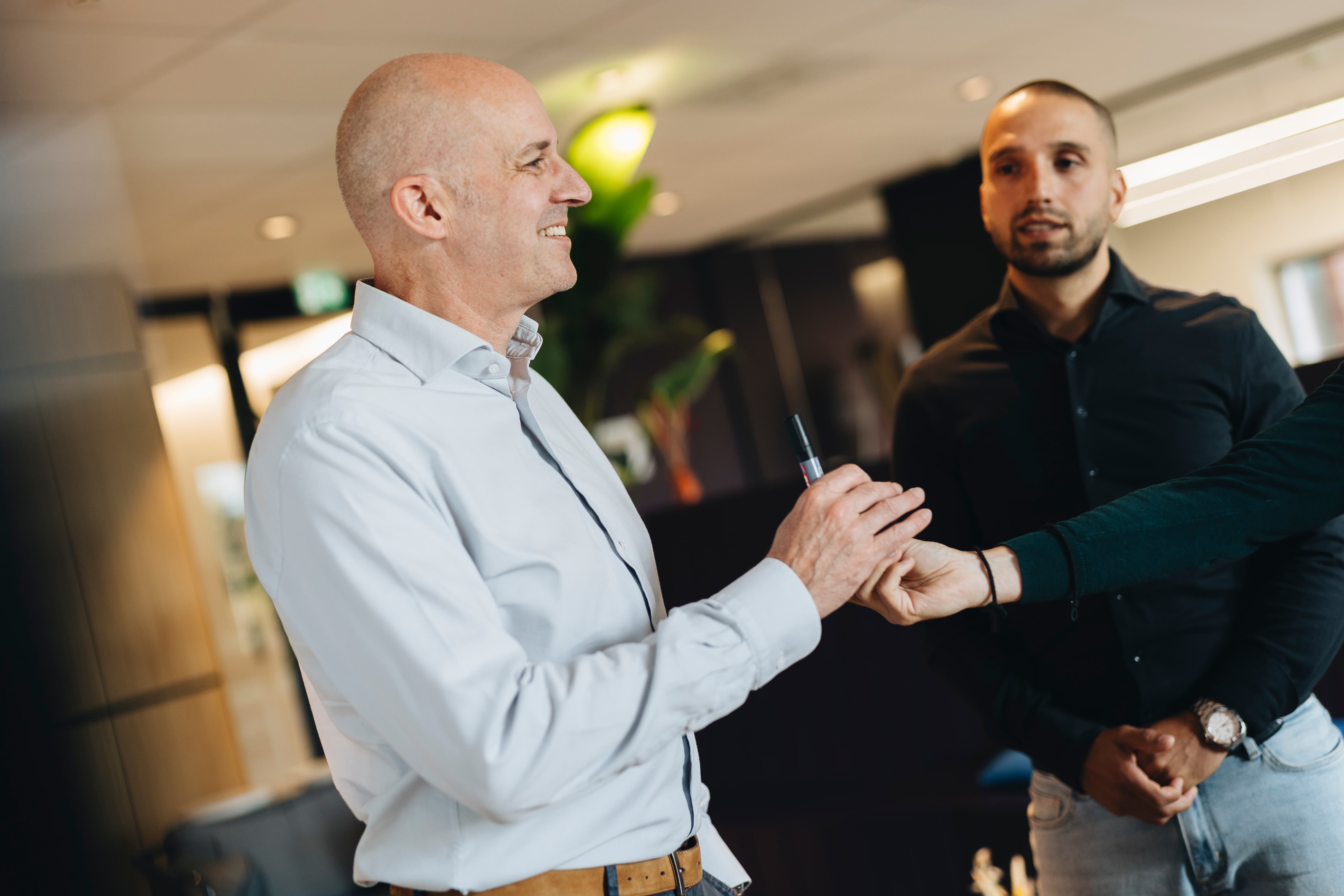 Twee mannen in gesprek in een kantooromgeving, terwijl één persoon een pen aanreikt. Zakelijke ontmoeting met teamoverleg en samenwerking