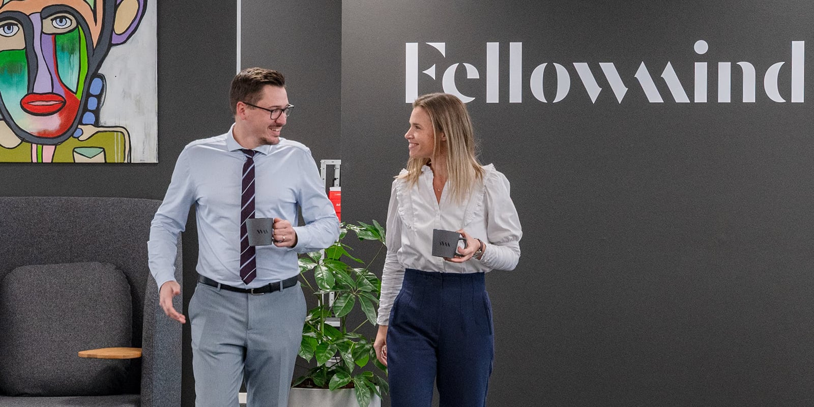 En mand og en kvinde går ved siden af hinanden med Fellowmind-kaffekopper i hænderne