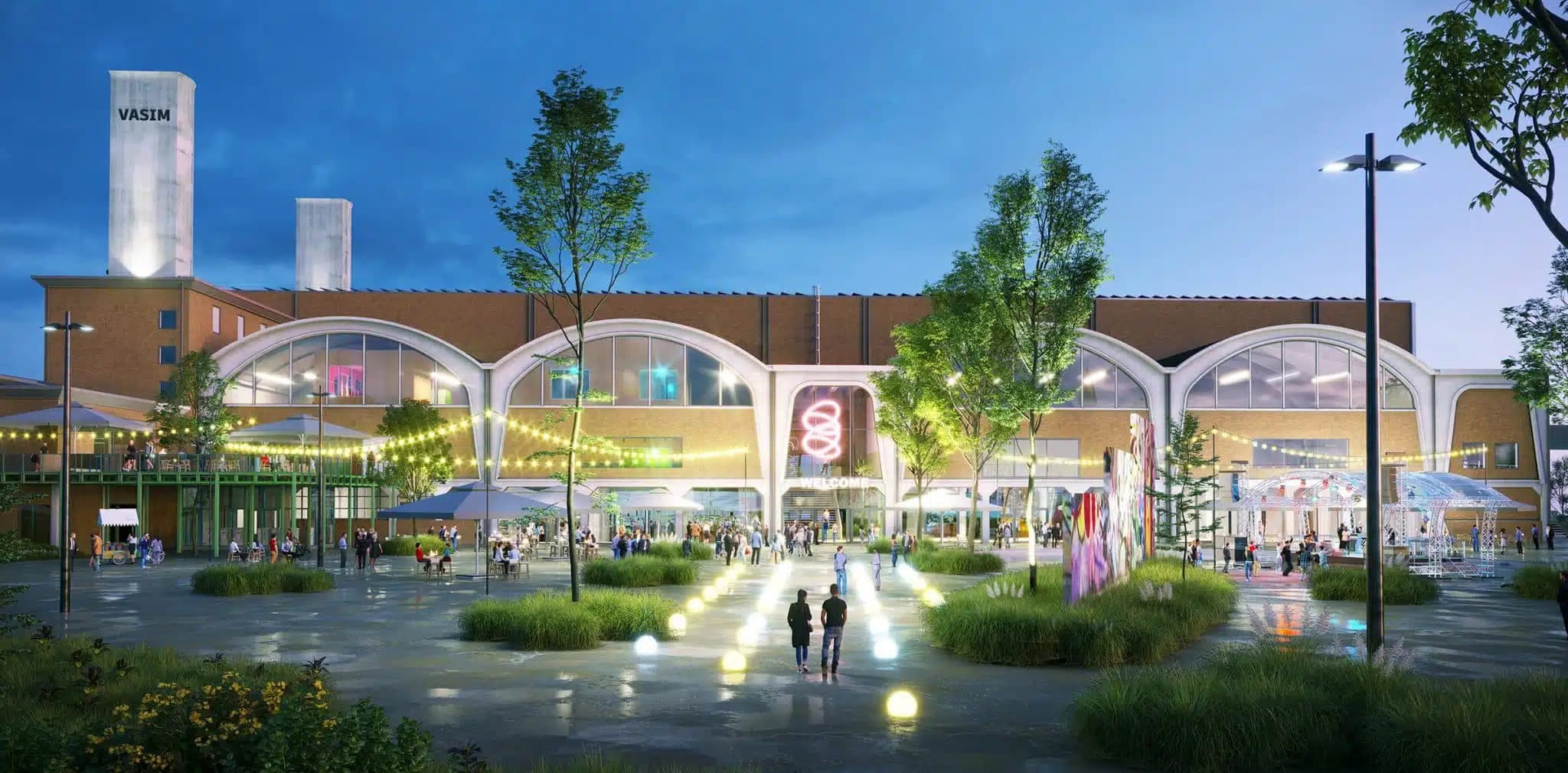 Avondbeeld van een modern winkel- en vrijetijdscentrum met verlichte gevels, bomen en een plein met bezoekers