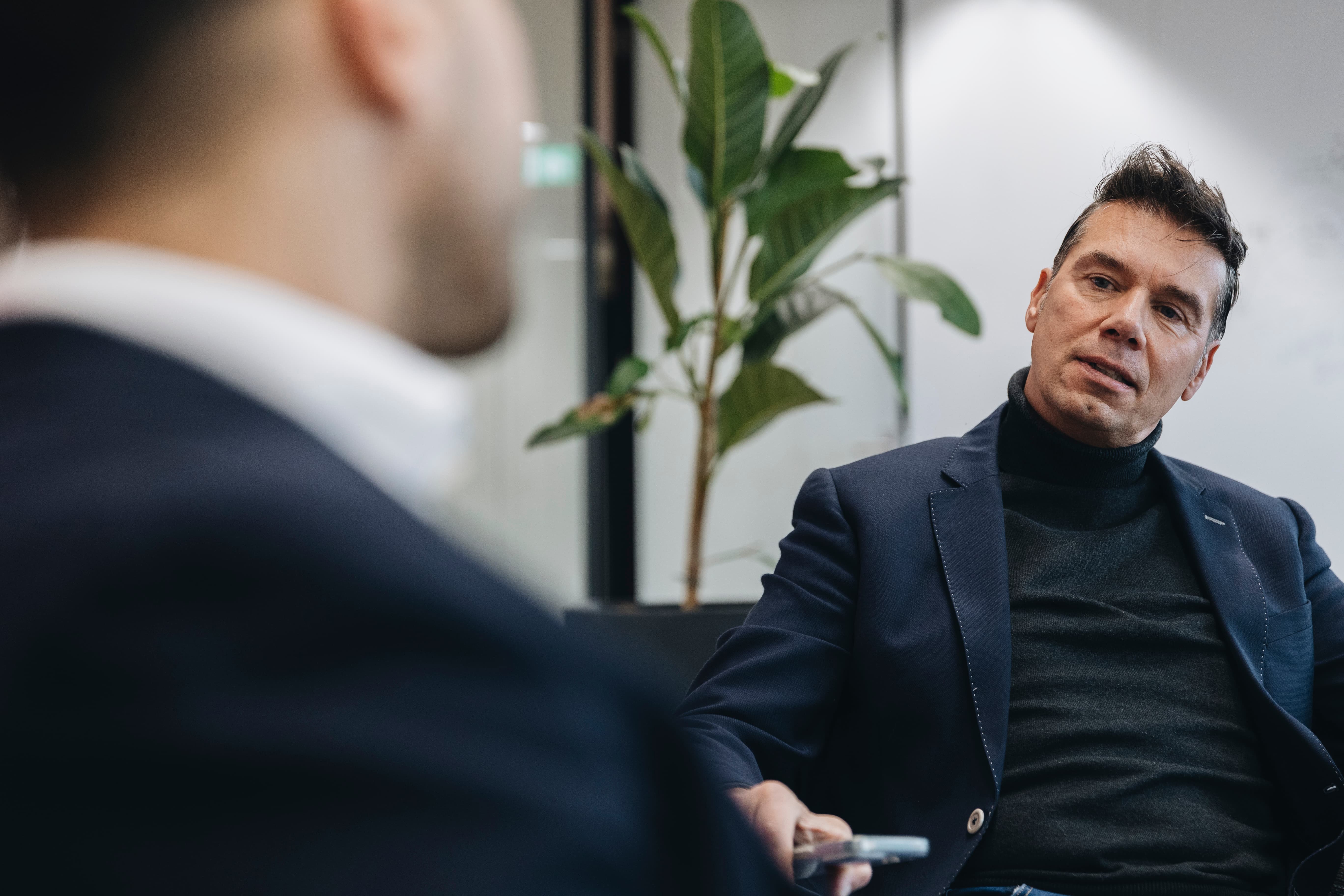 Twee mannen in gesprek tijdens een zakelijk kantooroverleg, met een plant op de achtergrond