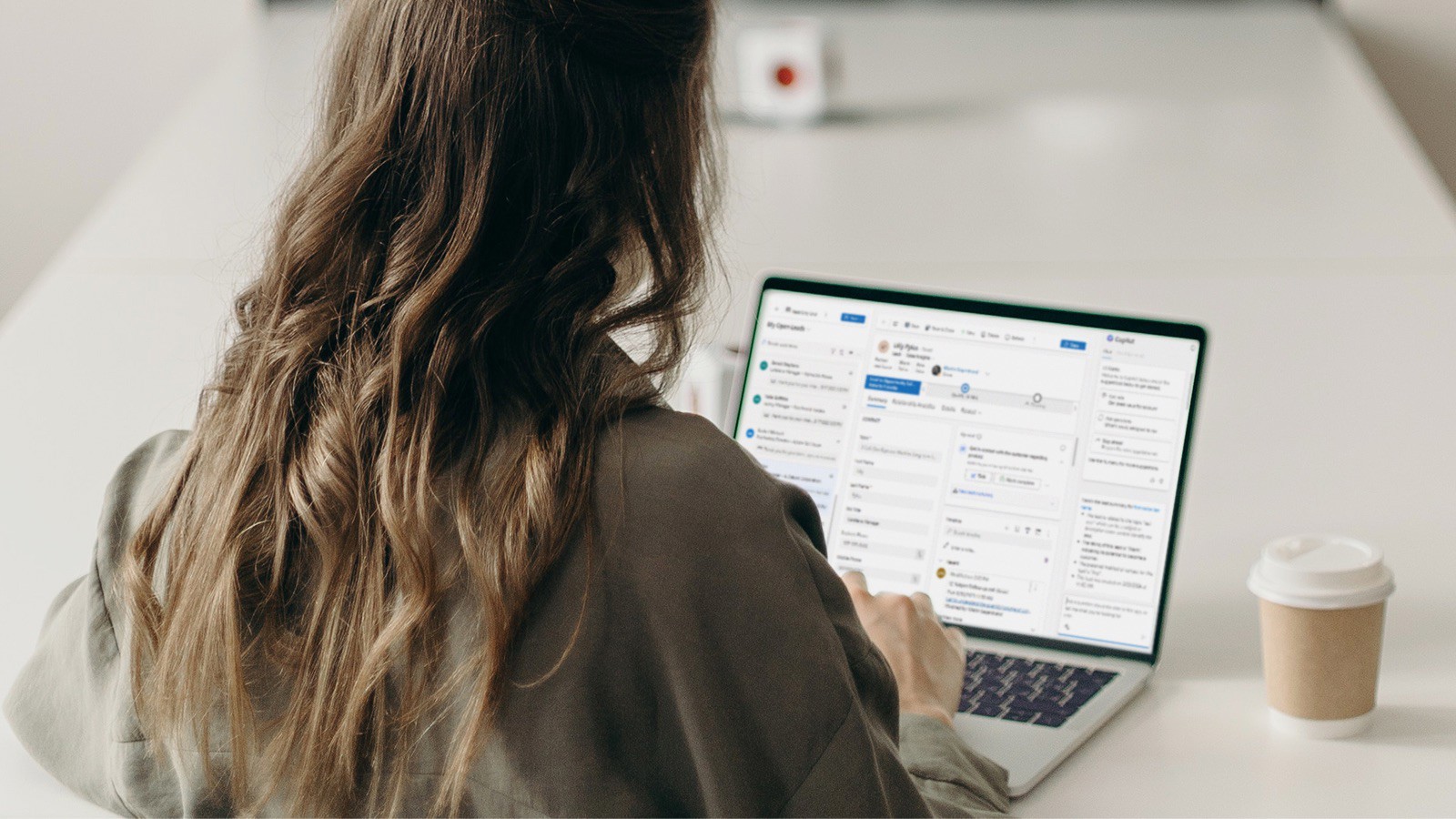 Person bakifrån som arbetar vid en laptop på ett skrivbord, med kaffe bredvid. Kontorsmiljö med fokus på digitalt arbete och produktivitet